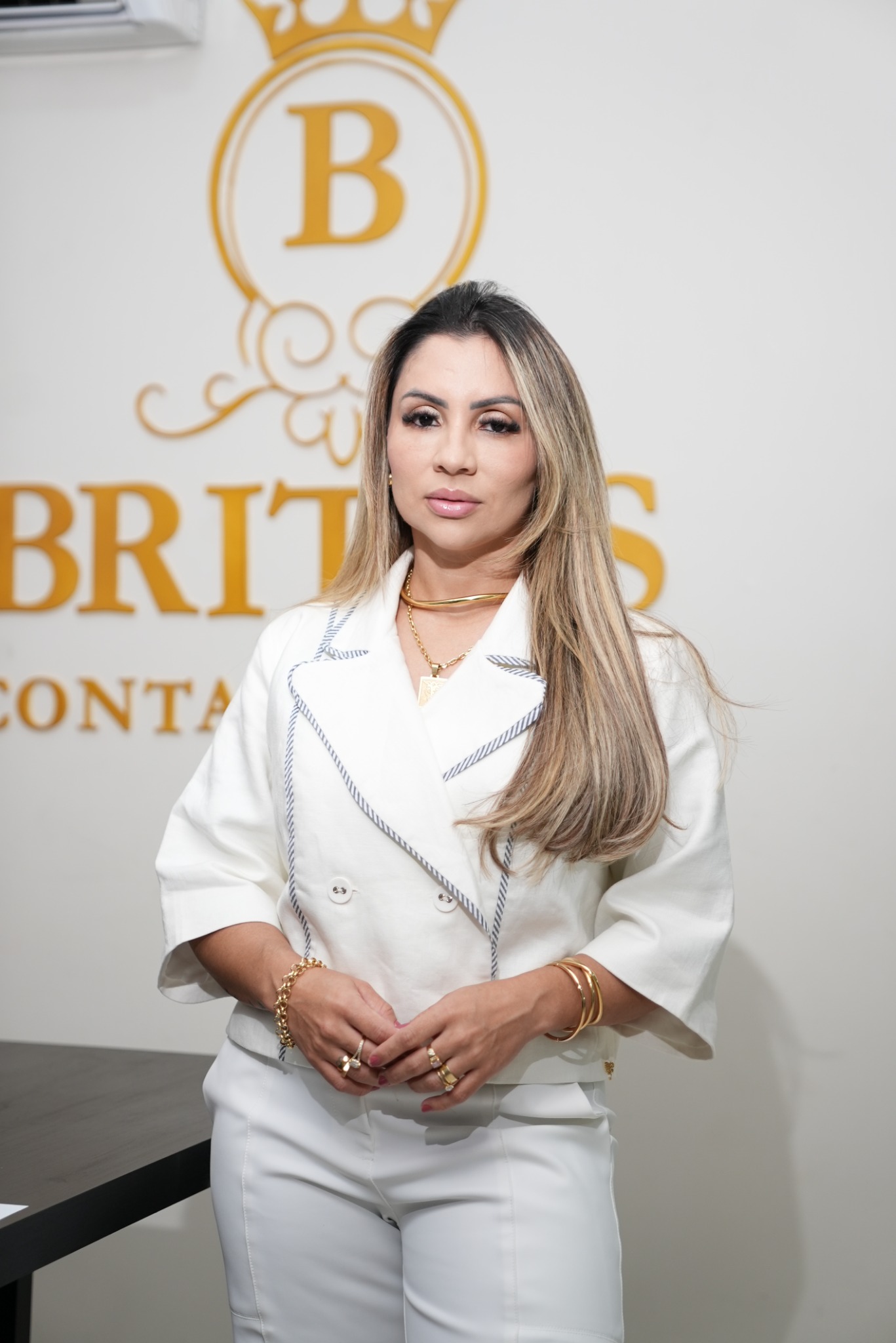 Julyana Britos em pé diante do letreiro dourado da Brito's Contabilidade.